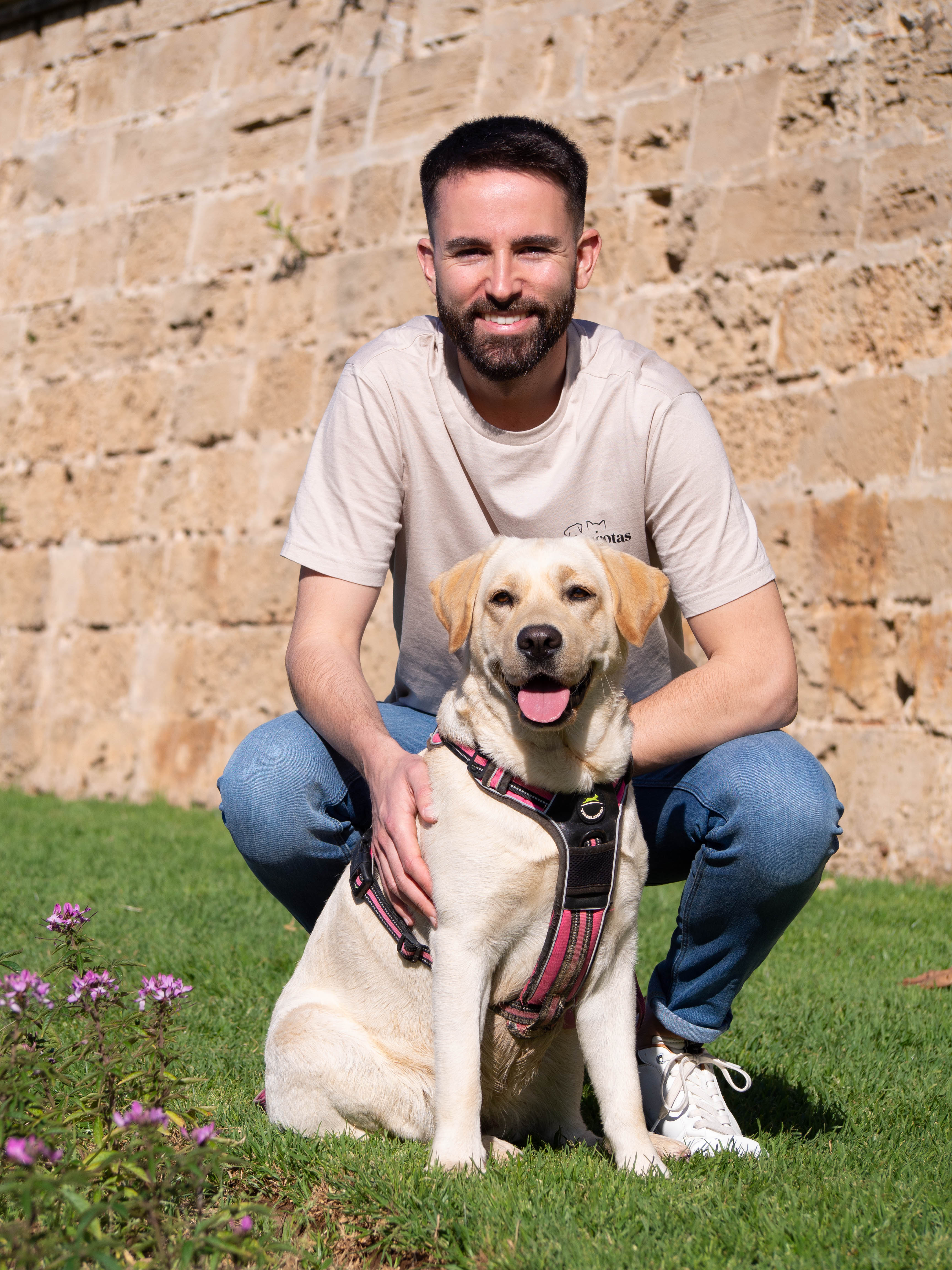 Enric agachado junto a Kalúa frente a un muro de piedra